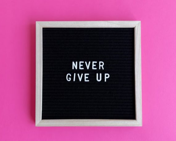 A framed letter board with 'NEVER GIVE UP' on a vibrant pink background.
